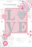 This anniversary card captures the tenderness of enduring romance, its design unfolding in a tranquil palette of pastel pinks and silvery greys reminiscent of a calm evening strolling through Enfield's quiet residential streets. At the centre sits the word LOVE, spelled in soft, raised glitter that lends both light and gentle texture. The letter O is transformed into a shimmering silver heart, subtly textured so it appears almost like a tiny piece of jewellery nestled in the middle of the card. Around this focal image, an array of delicate blooms unfurls in shades of blush, mauve, and ivory. The flowers are painted with an almost watercolour softness, their edges slightly blurred and their veins lightly traced, much like the refined petals we select for romantic arrangements for couples across Enfield. Fine swirls and tendrils weave through the blossoms, while discreet butterflies and scattered petals provide a sense of gentle movement, evoking the grace of an English spring garden after a light breeze drifts through. The soft pink background supports the design without overwhelming it, allowing the silver accents to sparkle subtly, like lamplight reflected on wet pavements near Enfield Town after a spring shower. Elegant script spells out On Our Anniversary and I love you today and always, the lettering flowing comfortably with the curves of the floral motif. The overall composition feels serene and heartfelt, as if this single card were a keepsake of shared journeys, whispered promises, and many anniversaries marked side by side in Enfield.